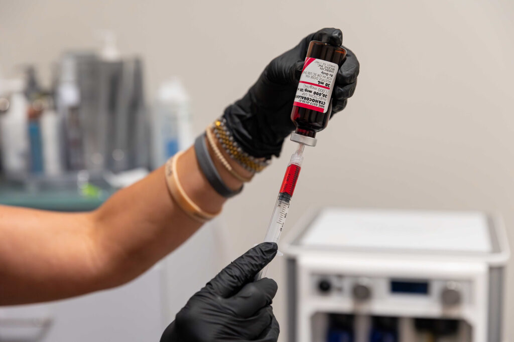 Close up of a medical provider preparing a syringe for vitamin injections in Homewood. Their gloved hands hold a bottle of the IV blend while removing some of the liquid with a syringe.