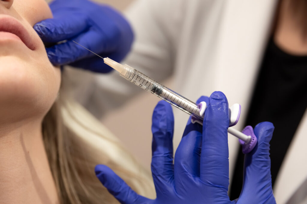 Close up of a professional with blue gloves injecting lip filler in Homewood into a female patient's lips