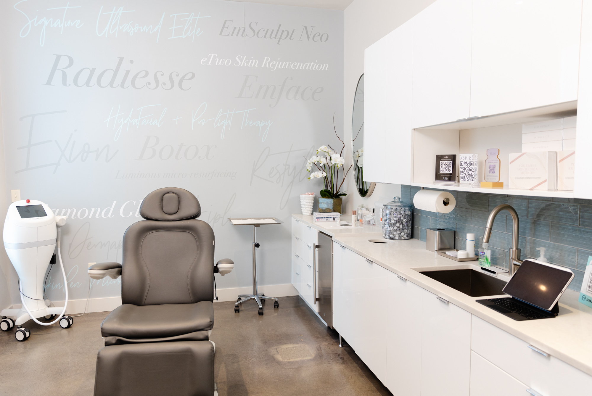 A clean, minimalistic treatment room containing a comfortable chair, medical device, and countertop at a medical practice, which you could visit after searching for a med spa near me.